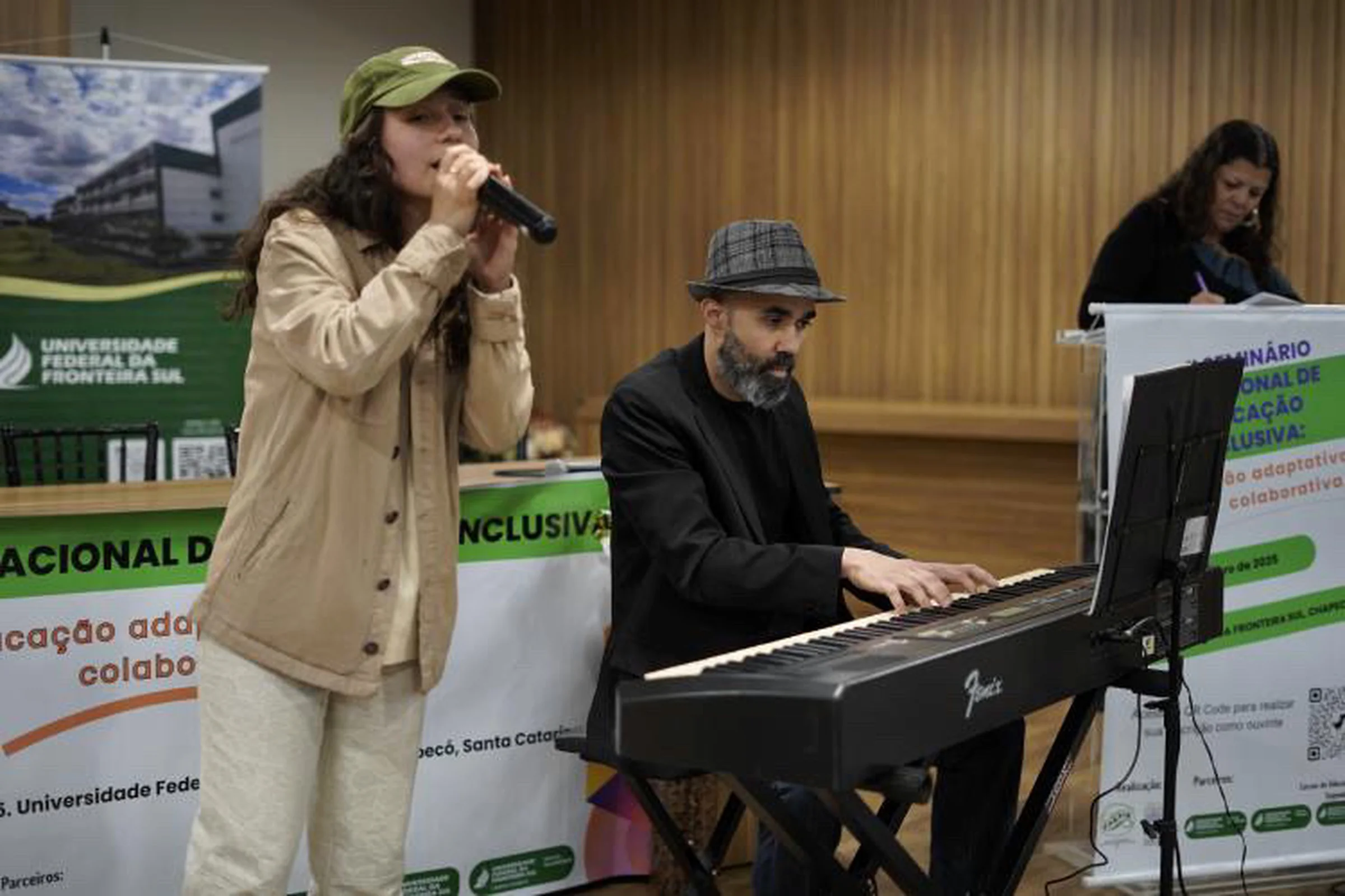 Karen canta ao microfone ao lado de um pianista, num seminário.