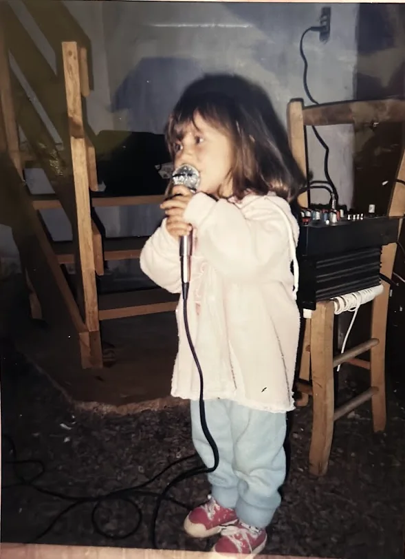 Fotografia antiga: Karen pequena canta ao microfone, ao lado de uma mesa de som.