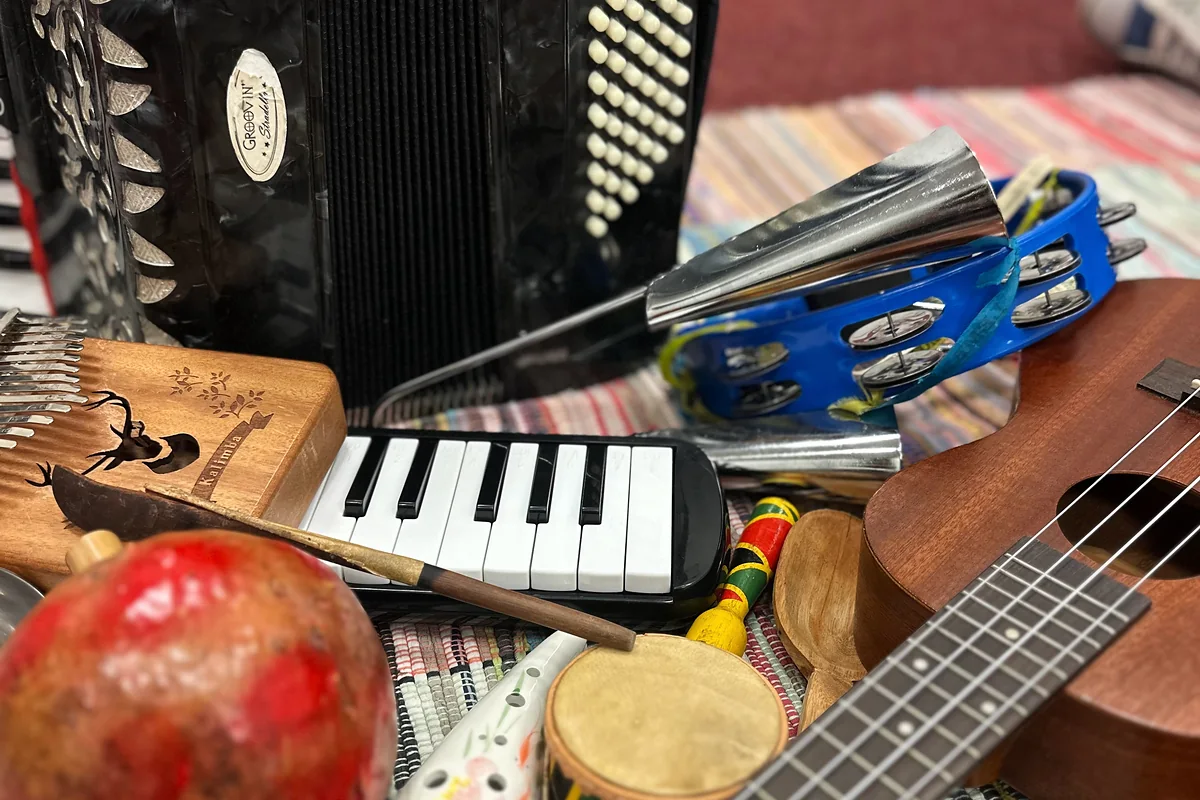 Acordeom, escaleta, ukulele, pandeiro e outros instrumentos sobre um tapete listrado.