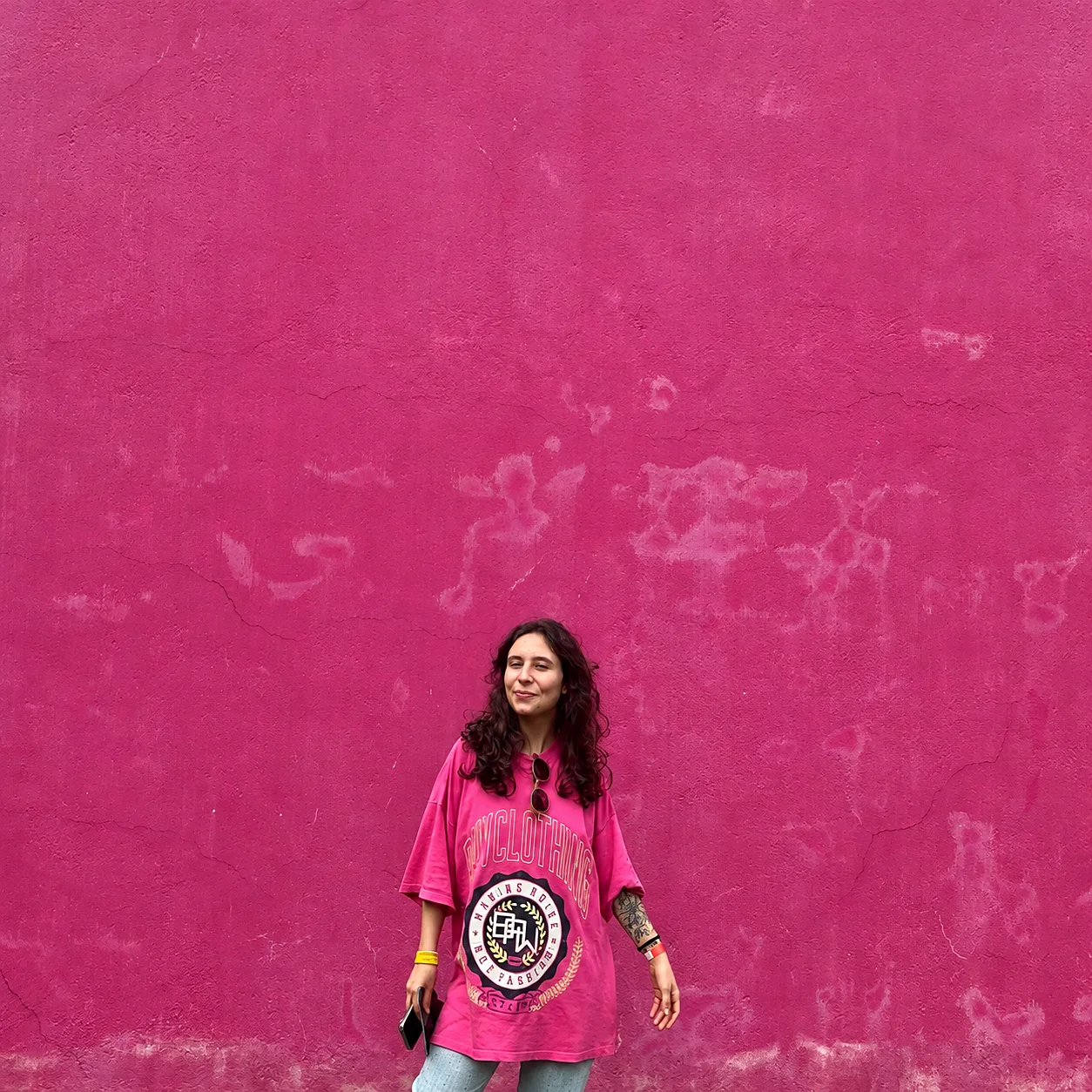 Karen de camiseta rosa diante de um muro pintado de rosa.