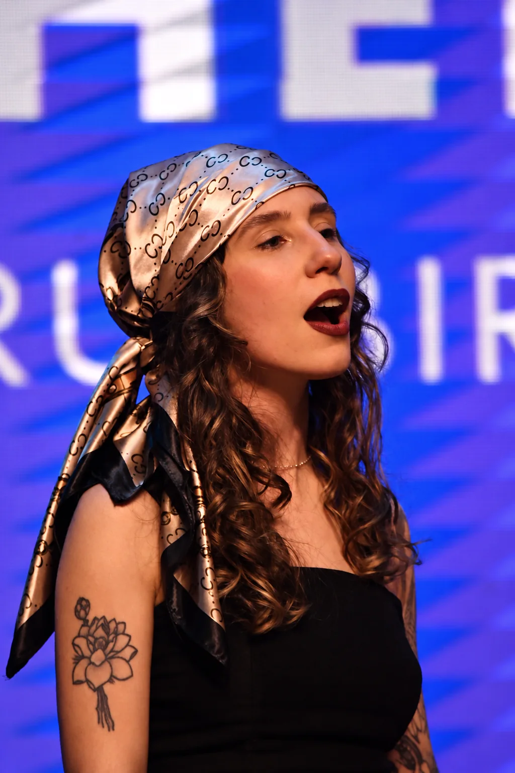 Karen canta com um lenço de seda no cabelo, diante de um telão azul.
