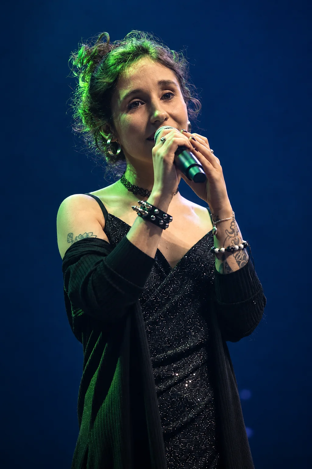 Karen canta ao microfone num palco escuro, sob luz verde.