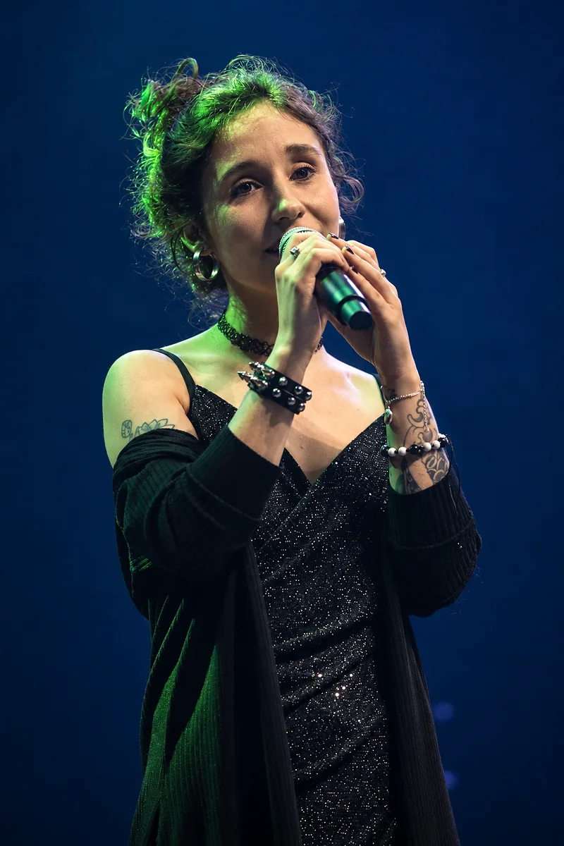 Karen canta ao microfone num palco escuro, sob luz verde.