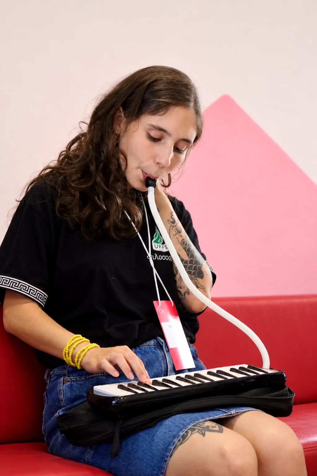 Karen toca escaleta sentada num sofá vermelho, numa sala de paredes rosadas.